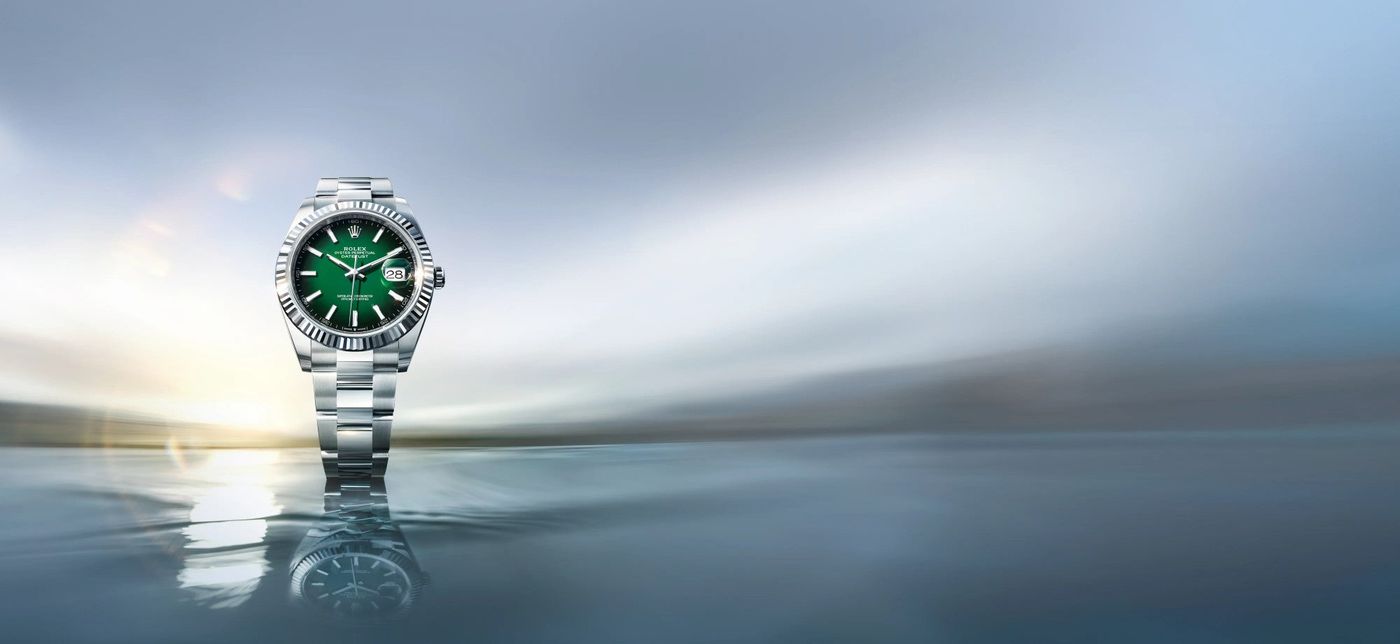 A Rolex Datejust with a green dial photographed against a soft sky reflection